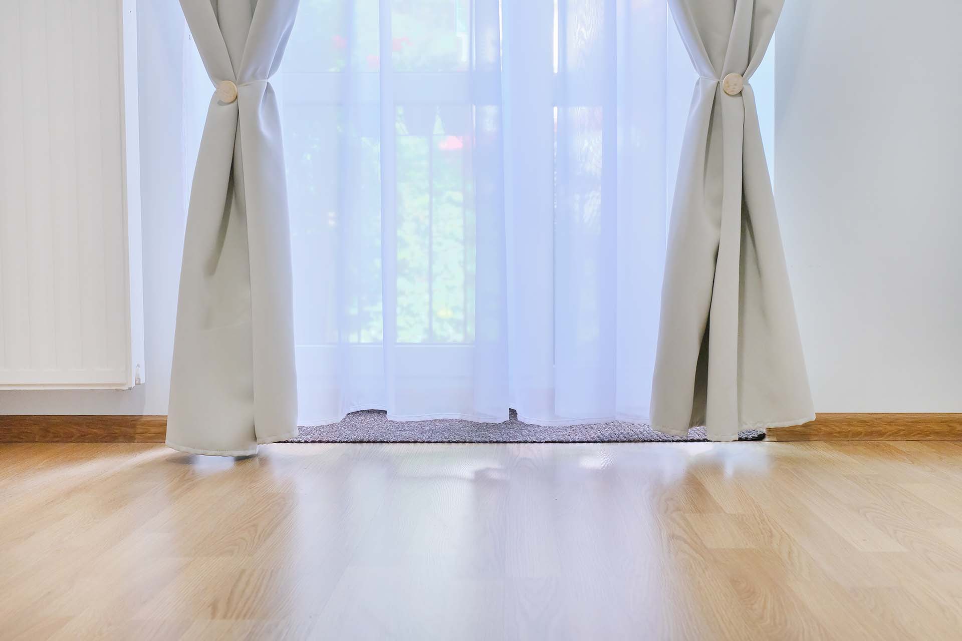 Interior details close up. Brown wood laminate, glass balcony door with gray white curtains, copy space floor
